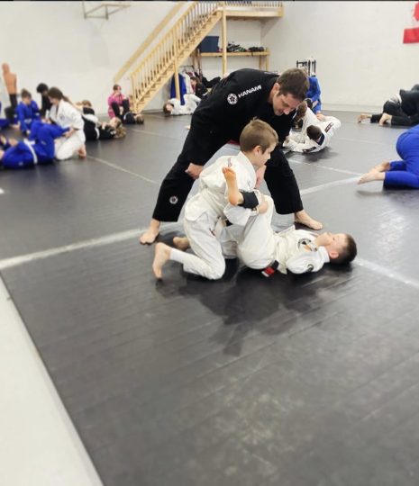 A coach guiding a young student through a technique on the mat