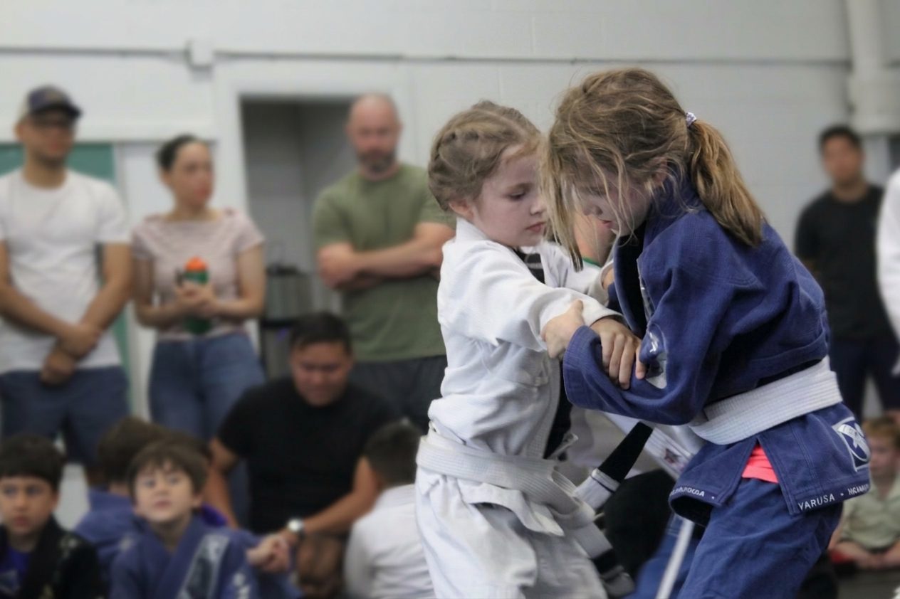 Two girls grip fighting while parents watch from the side