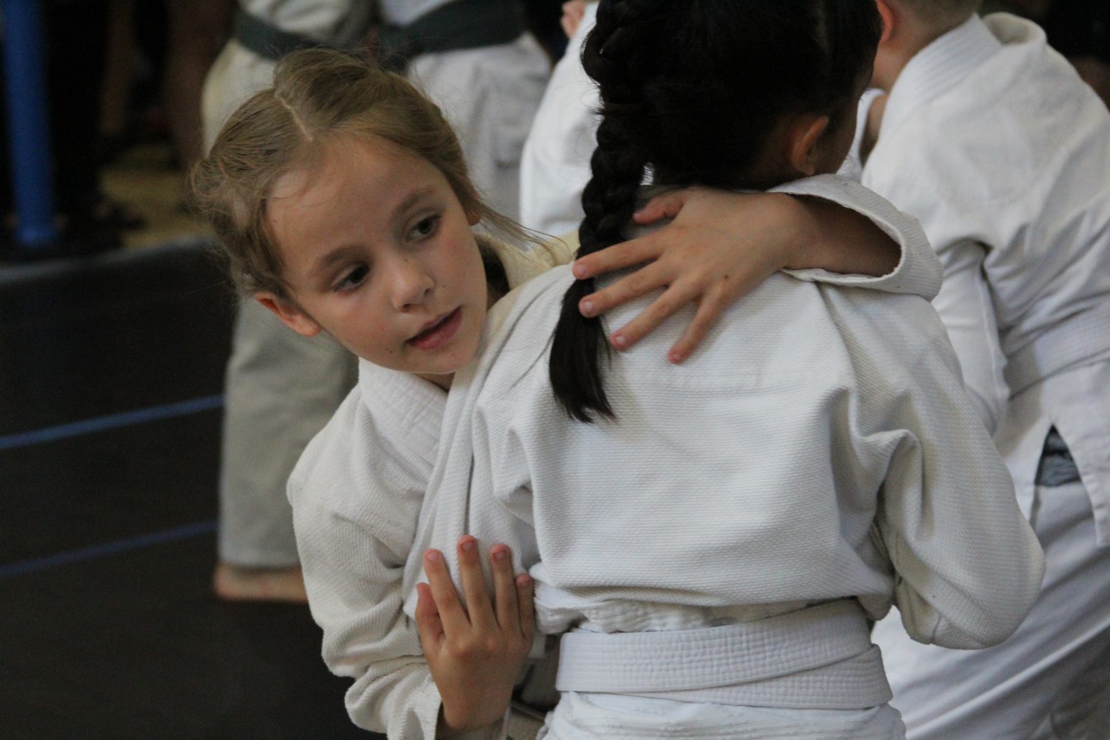 Two young students in white gis sharing a hug on the mat