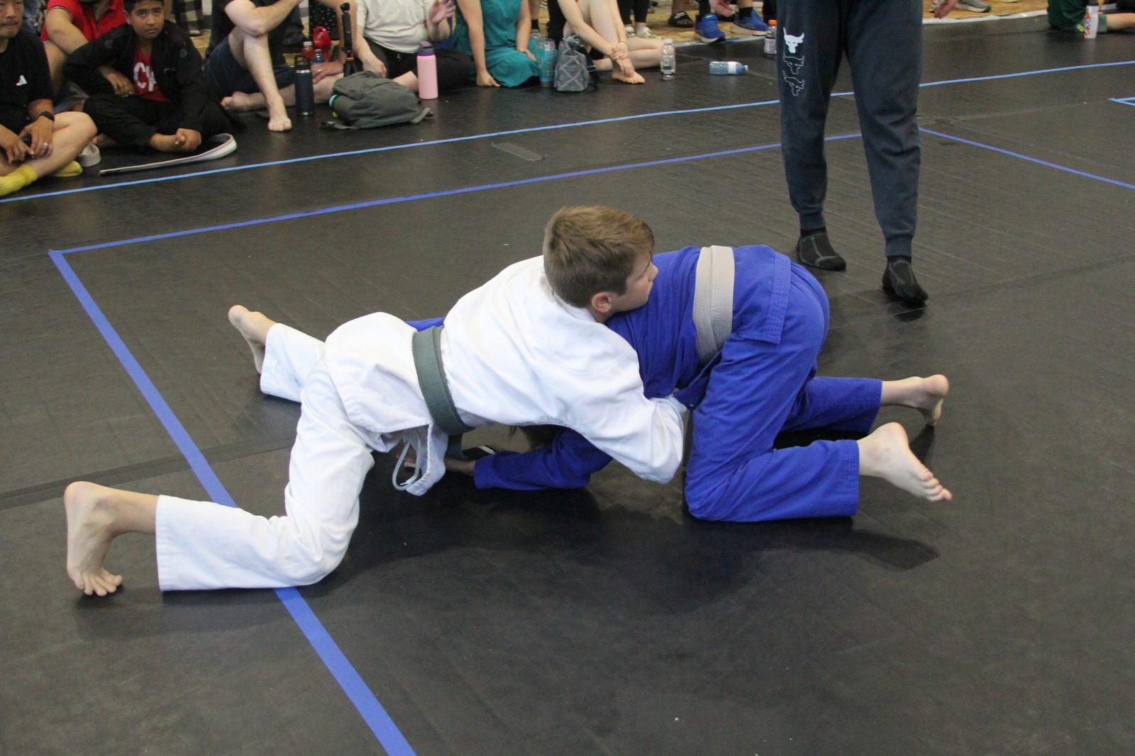 Two youth students in blue and white gis grappling on the mat